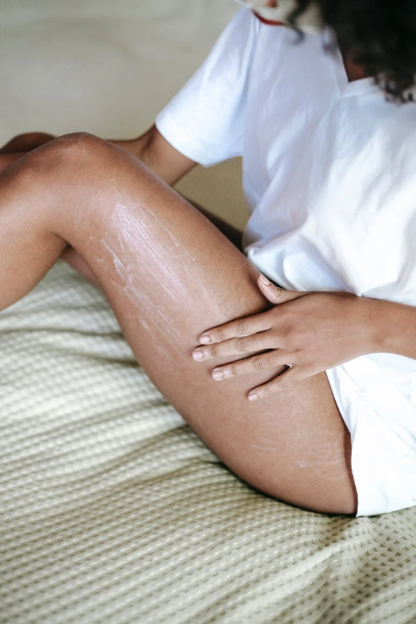 A woman applies moisturizer to her leg