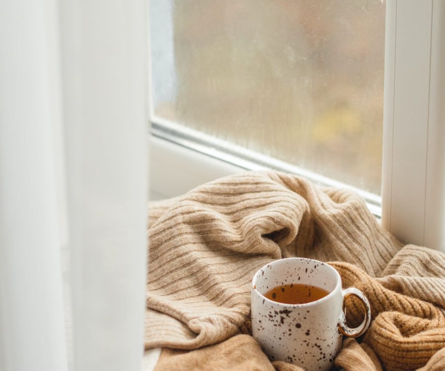 A cup of tea nestled in a blanket on a window sill
