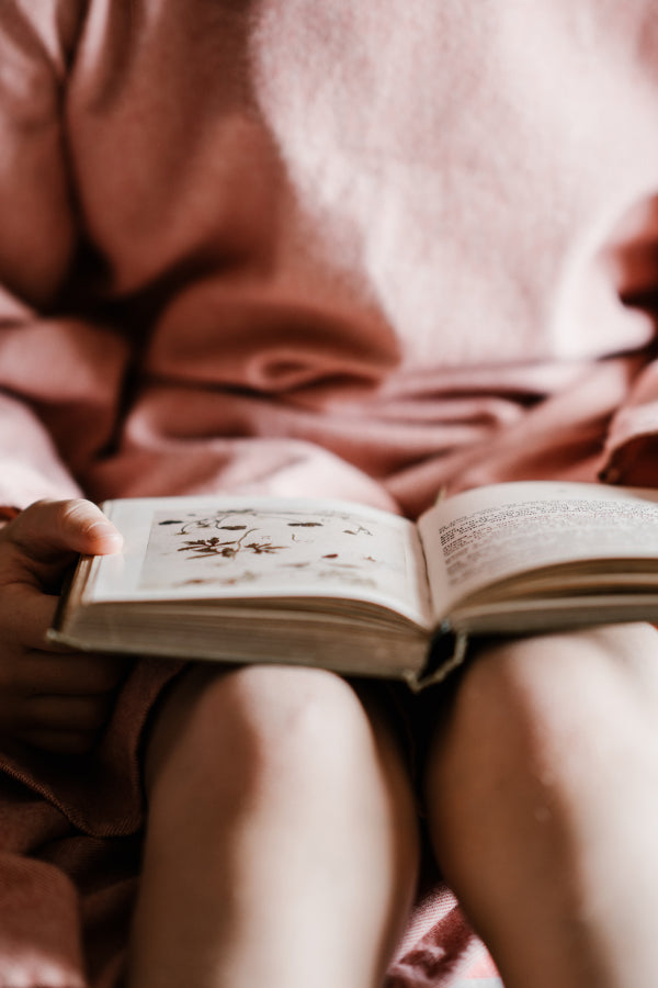 A kid in a pink sweater reads a book on their lap
